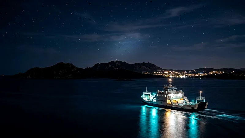 Lit ferry crossing dark water from Palau toward La Maddalena at night.