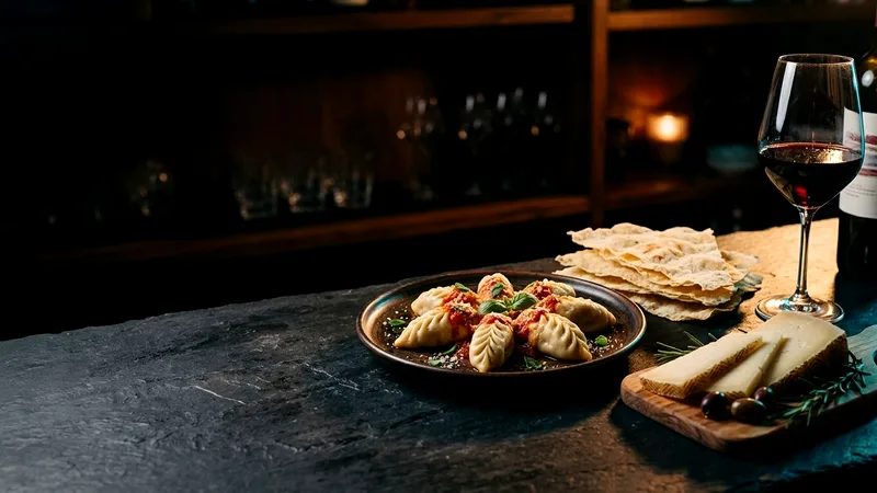 Pane carasau, culurgiones, pecorino and red wine on a dark counter.