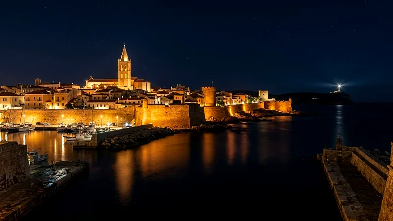 Alghero's lit sea walls and cathedral spire reflected in the night sea.